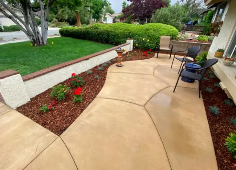 Curved tan colored-concrete walkway and patio beside planted beds