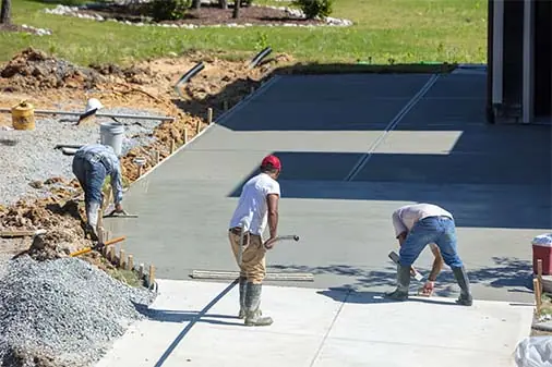 Three-person crew raking base and finishing a new slab next to the house