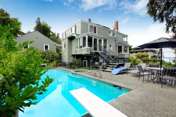 Concrete pool deck around a backyard pool with a diving board